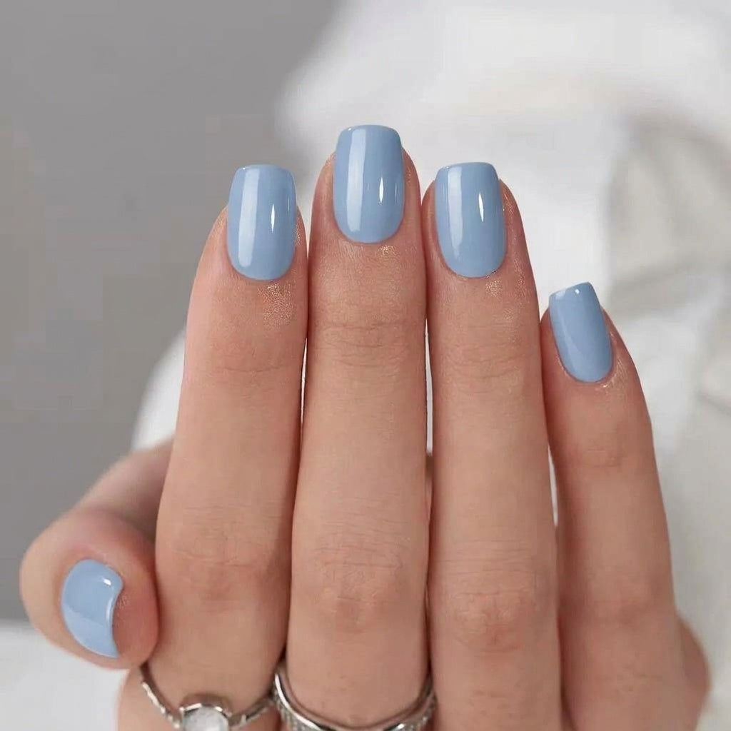 Närbild på fyra fingrar med Baby Blue press-on naglar i mjuk ljusblå och blank finish mot vitt tyg