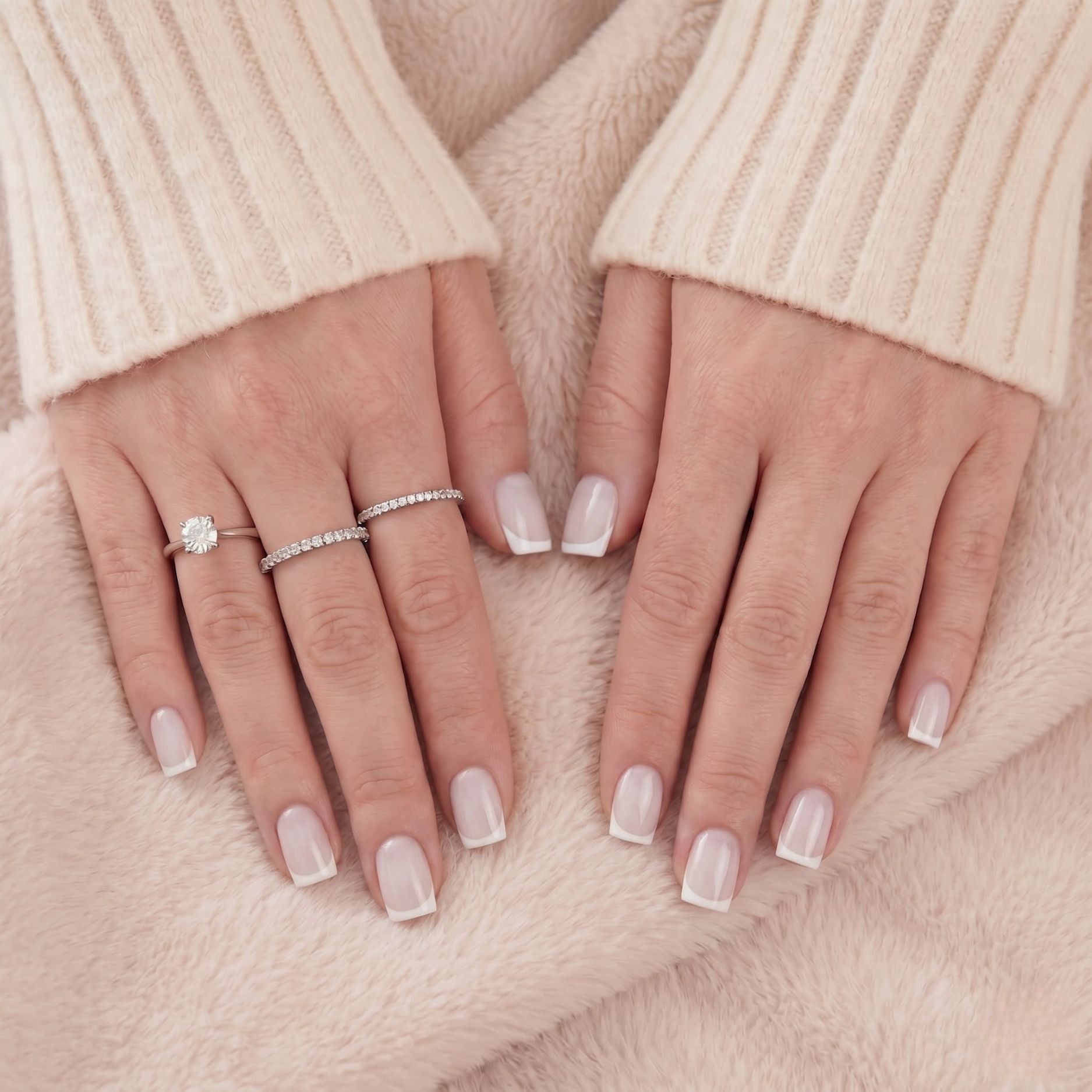 Close-up van witte Franse korte vierkante press-on nagels en zilveren ringen tegen beige vacht