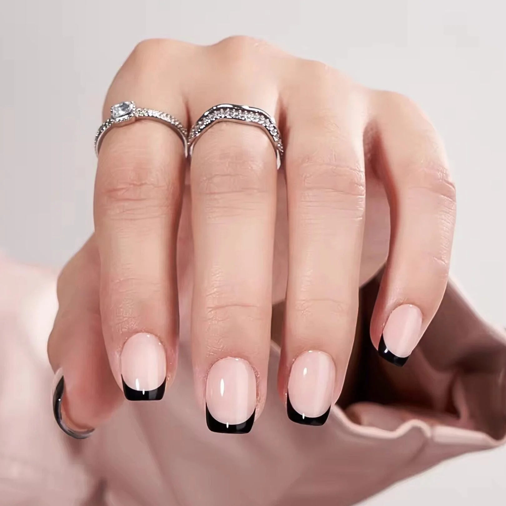 Sleek Silhouette press-on nagels close-up – zwarte Franse vierkante plaknagels met zilveren ringen tegen satijn