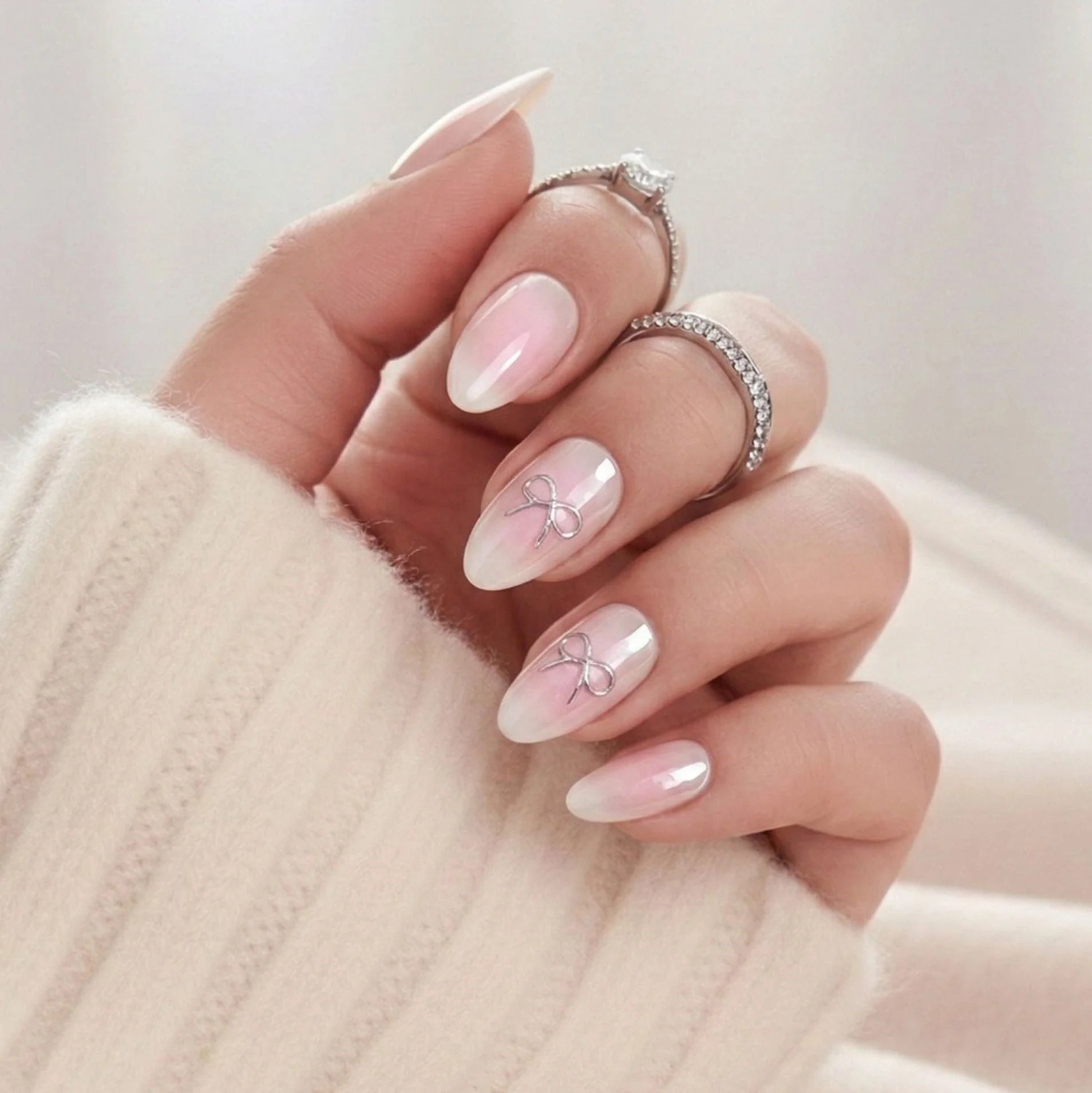 Aura Amoré press-on nagels – roze aura met zilveren strik-accent in amandelvorm tegen crème gebreide trui