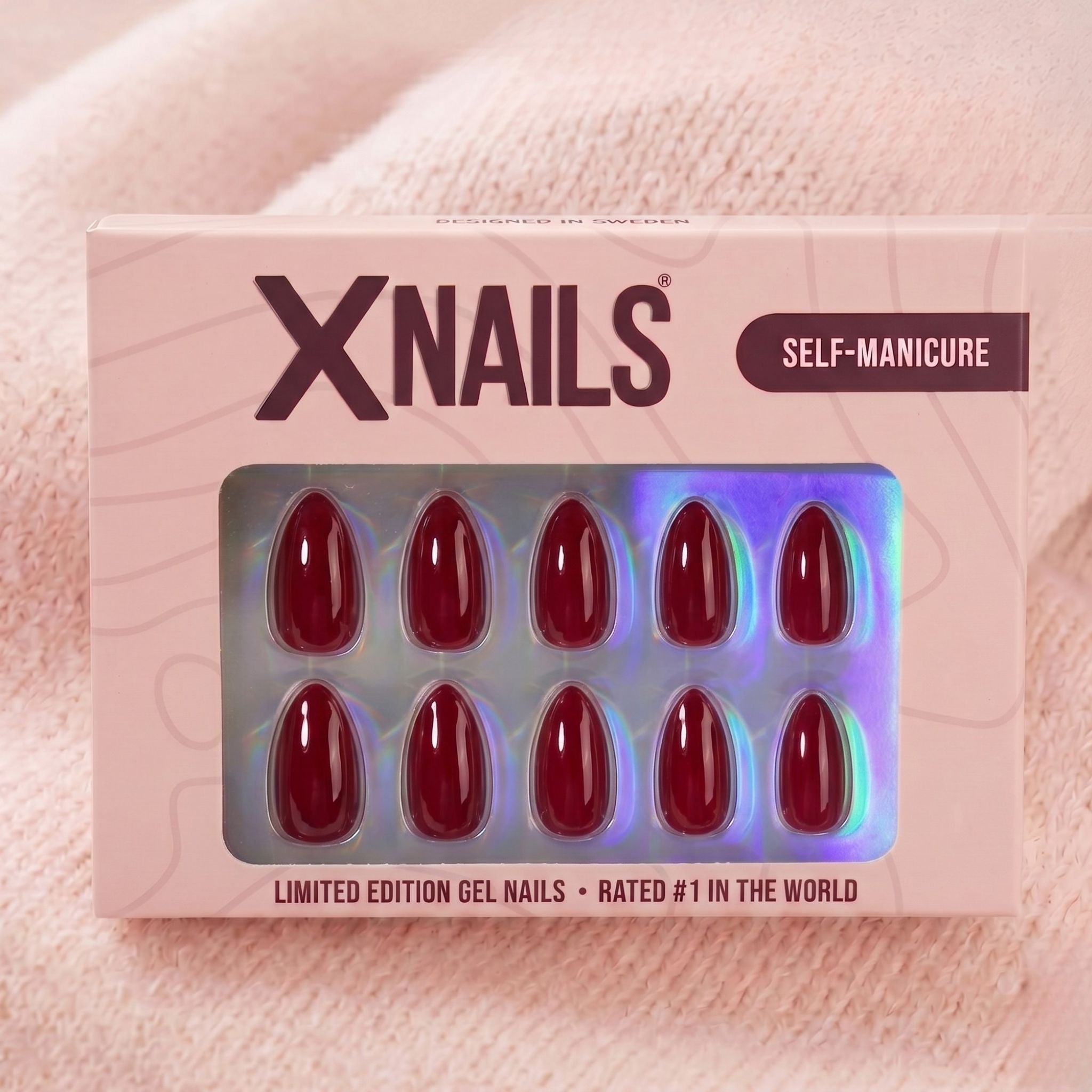 XNails-verpakking met wijnrode amandelvormige press-on nagels tegen roze gebreide achtergrond
