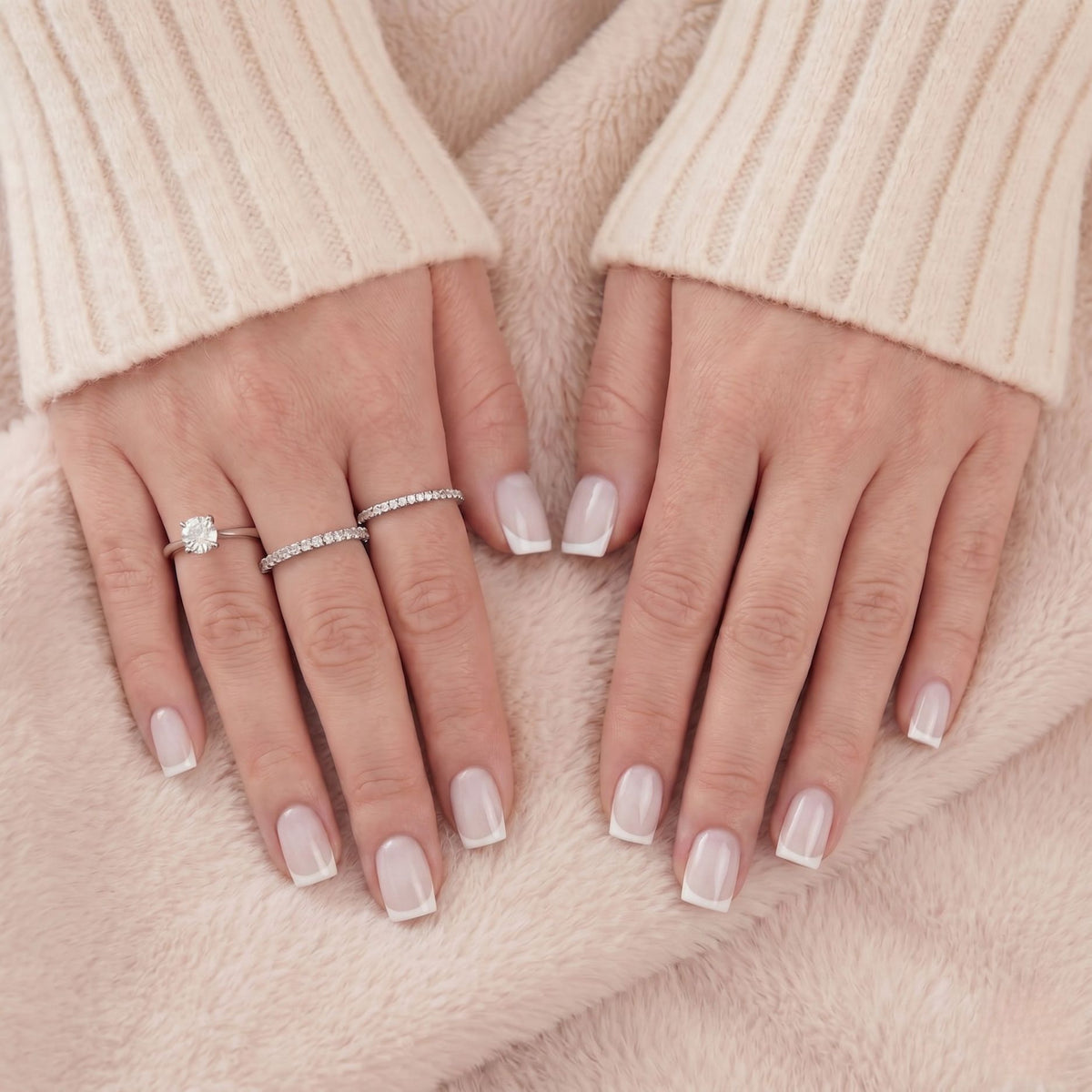 Close-up van witte Franse korte vierkante press-on nagels en zilveren ringen tegen beige vacht