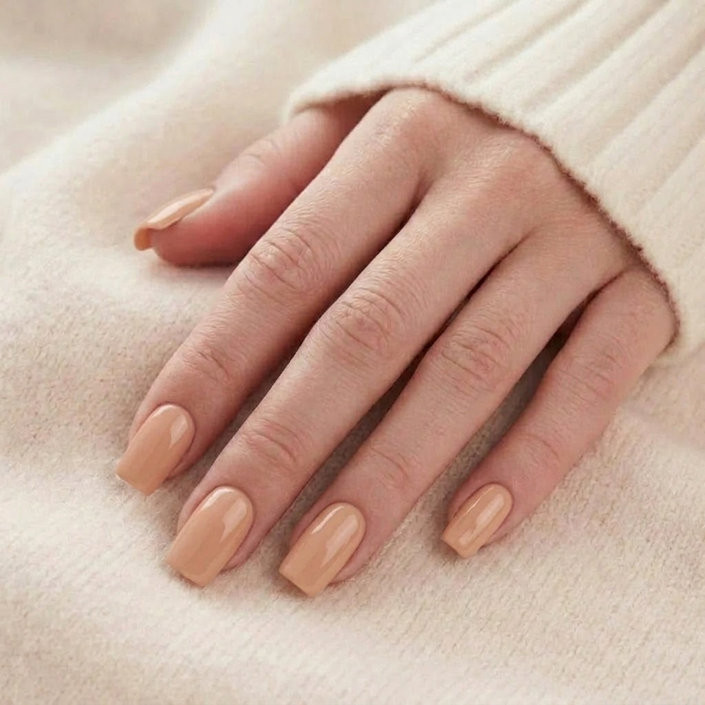 Honey Heaven press-on nagels in een effen nude/honingtint op een hand tegen een beige gebreide trui