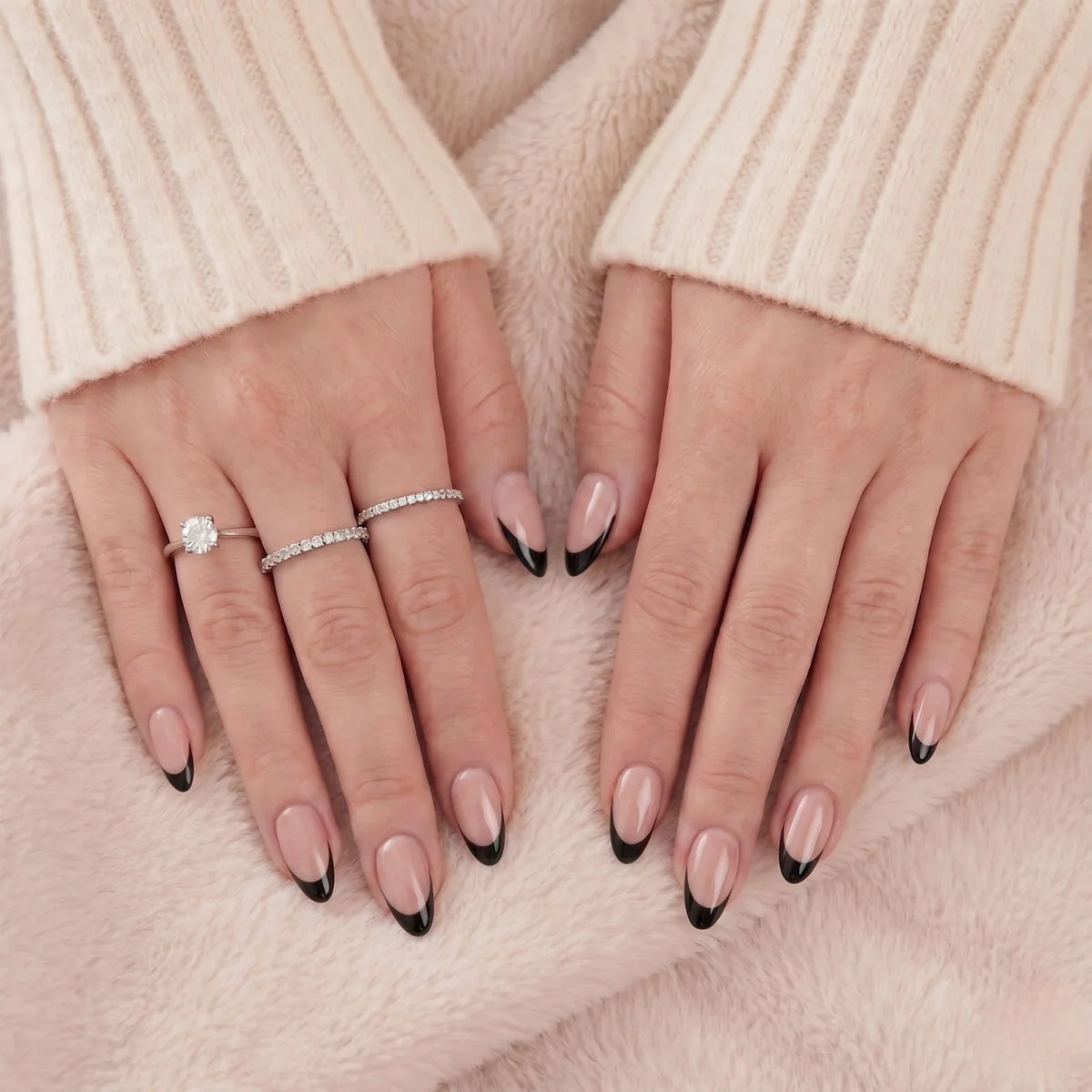 Zwarte Franse almond press-on nagels met zilveren ringen tegen een beige vacht