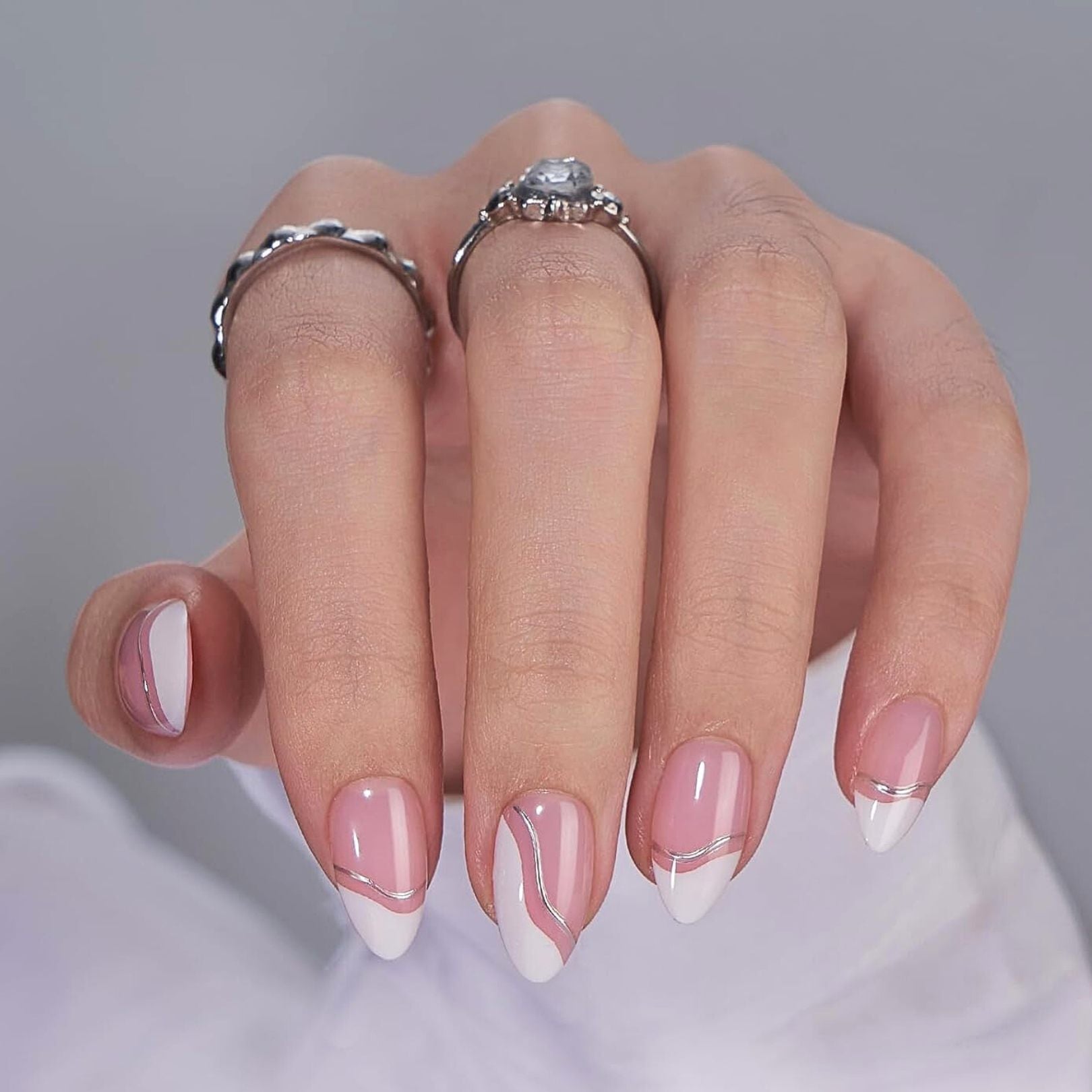 Nude beige press-on nagels – amandelvorm met natuurlijke glanzende finish op hand met zilveren ringen