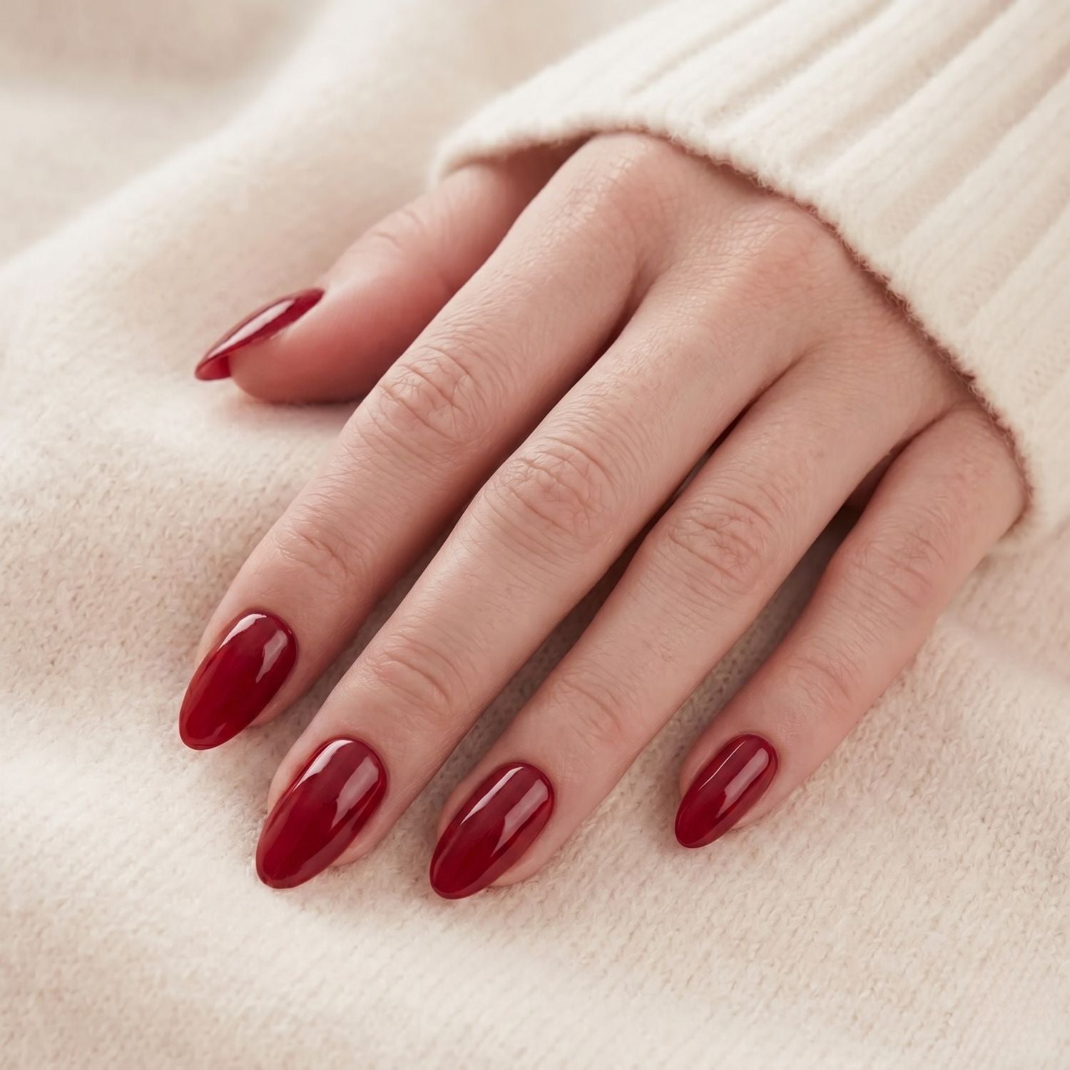 Ruby Romance nepnagels: wijnrode amandelvormige press-on nagels op hand tegen crèmewitte trui, chique manicure