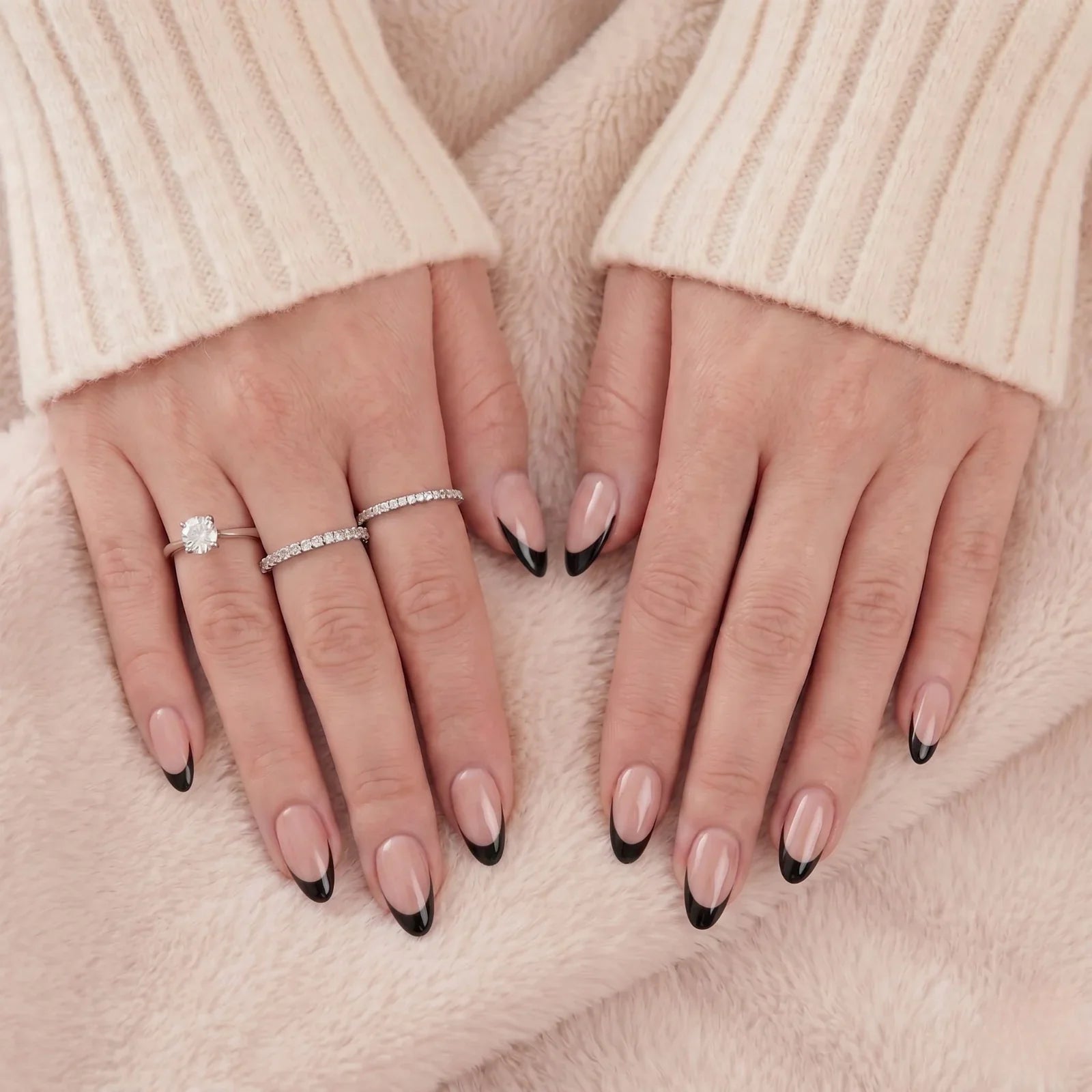 Zwarte Franse almond press-on nagels met zilveren ringen tegen een beige vacht