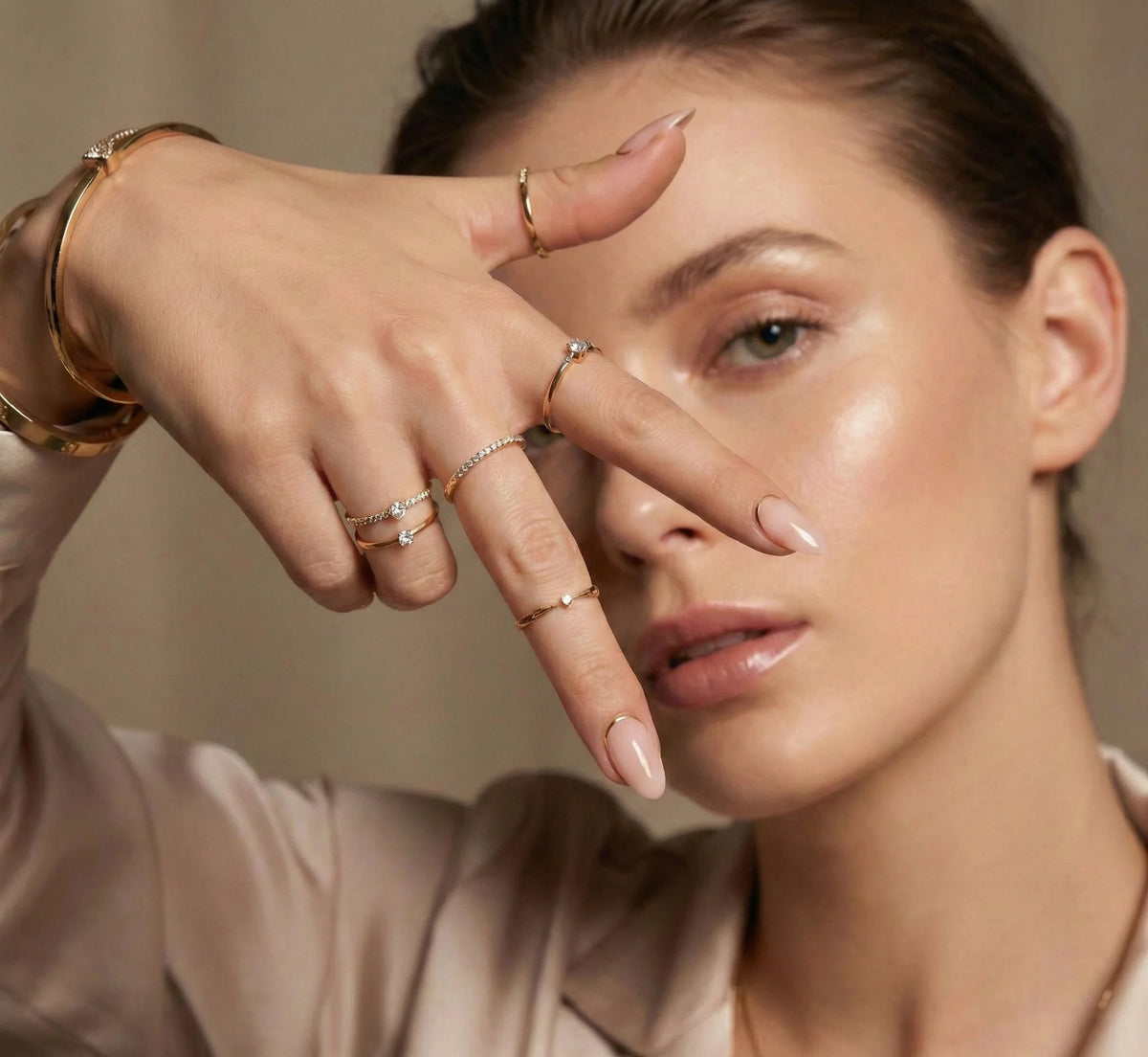 Elegant model toont amandelvormige nude press-on nagels met gouden rand en gouden ringen.