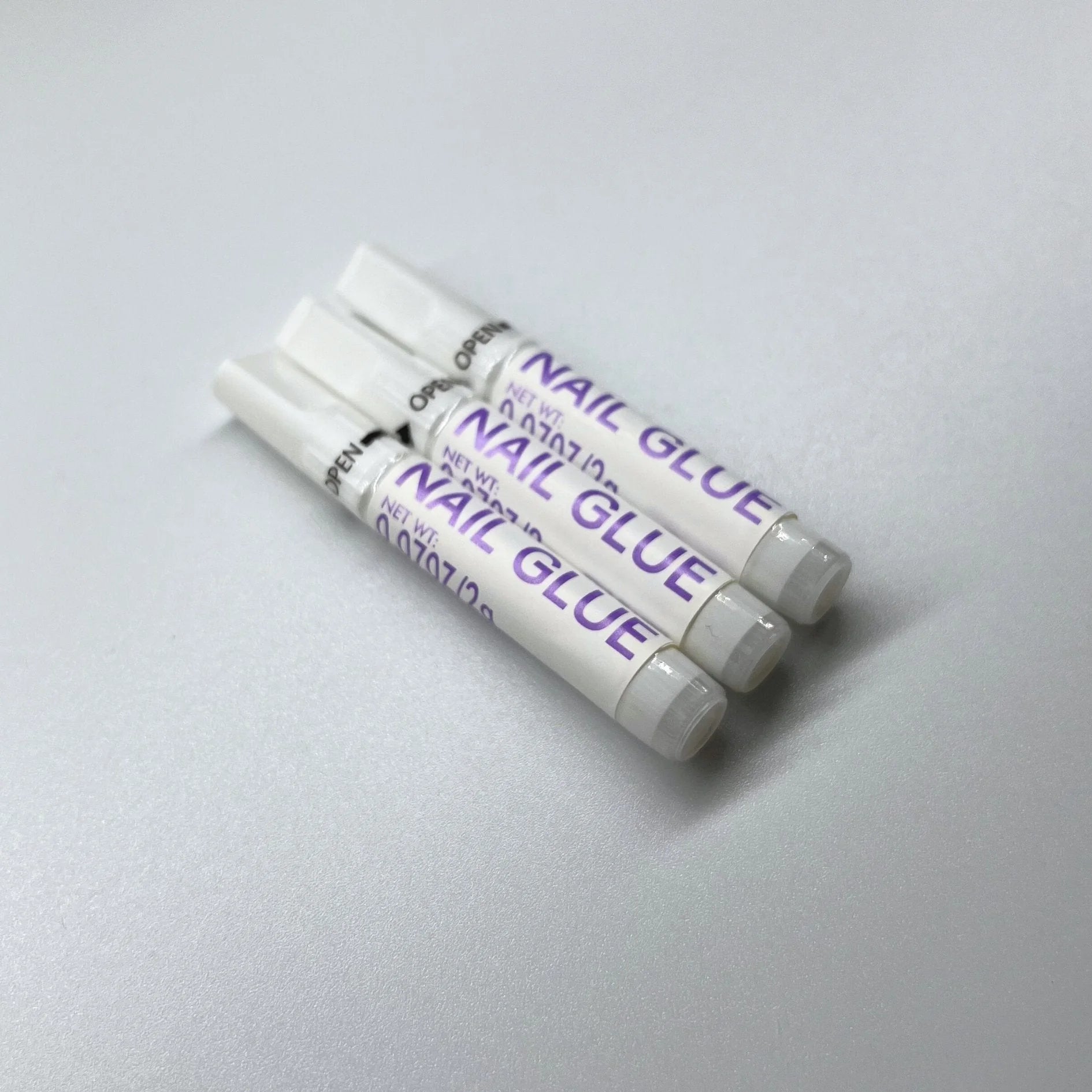 XGlue nagellijm close-up – drie tubes Nail Glue met open-pijl en applicatortip