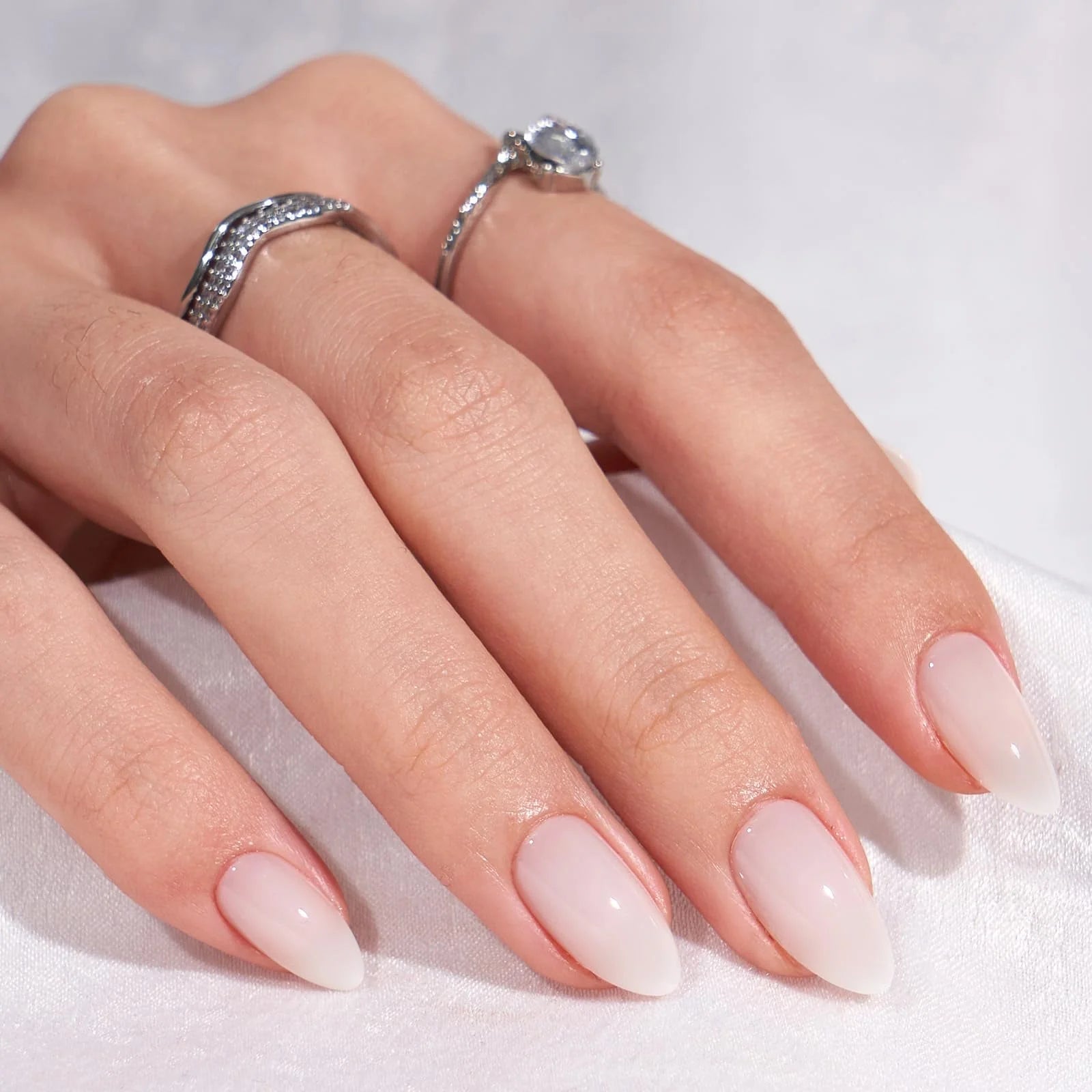 Amandelvormige gelnagels – Satin Snow in melkwit nude met zilveren ringen en kristal