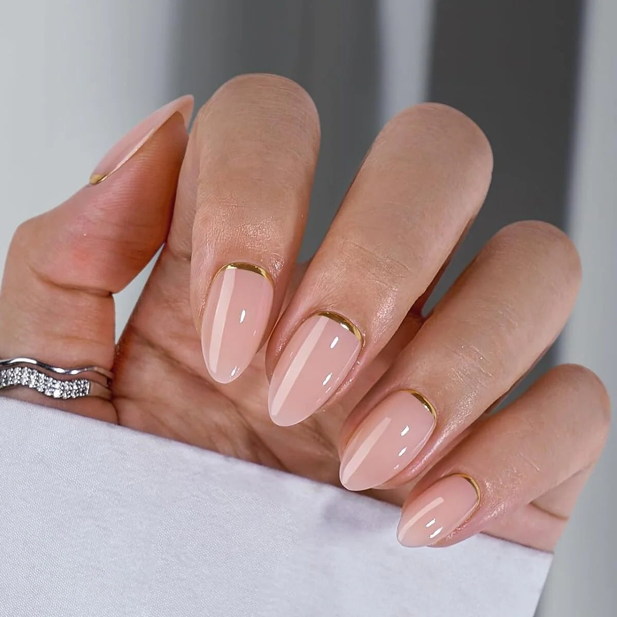 Golden Glimmer gelnagels close-up – nude amandel met gouden detail en zilveren ring