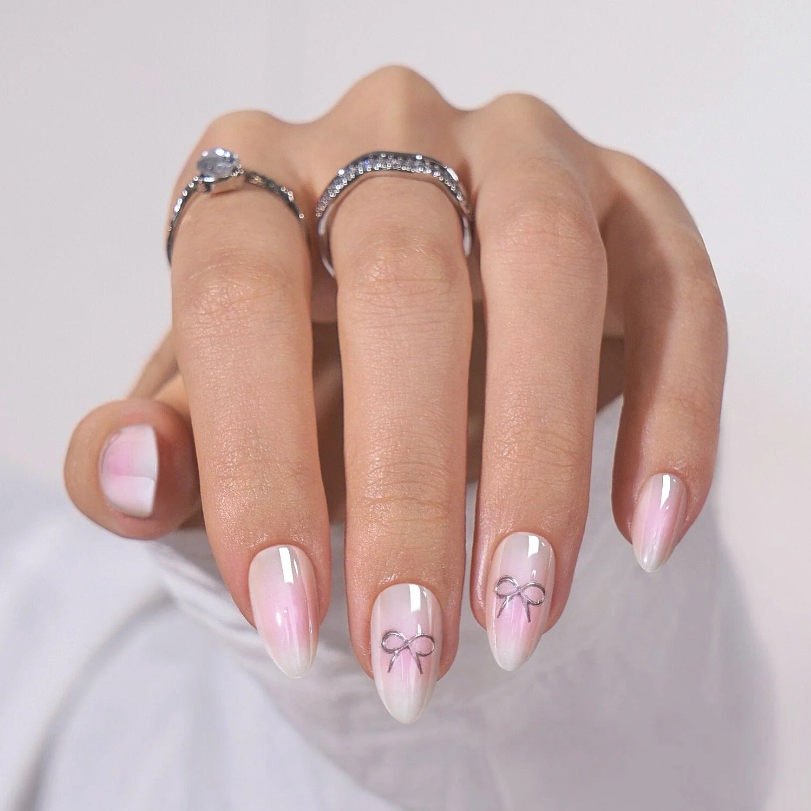 Aura Amoré nagels op hand – roze-witte aura met zilveren strik-detail en zilveren ringen