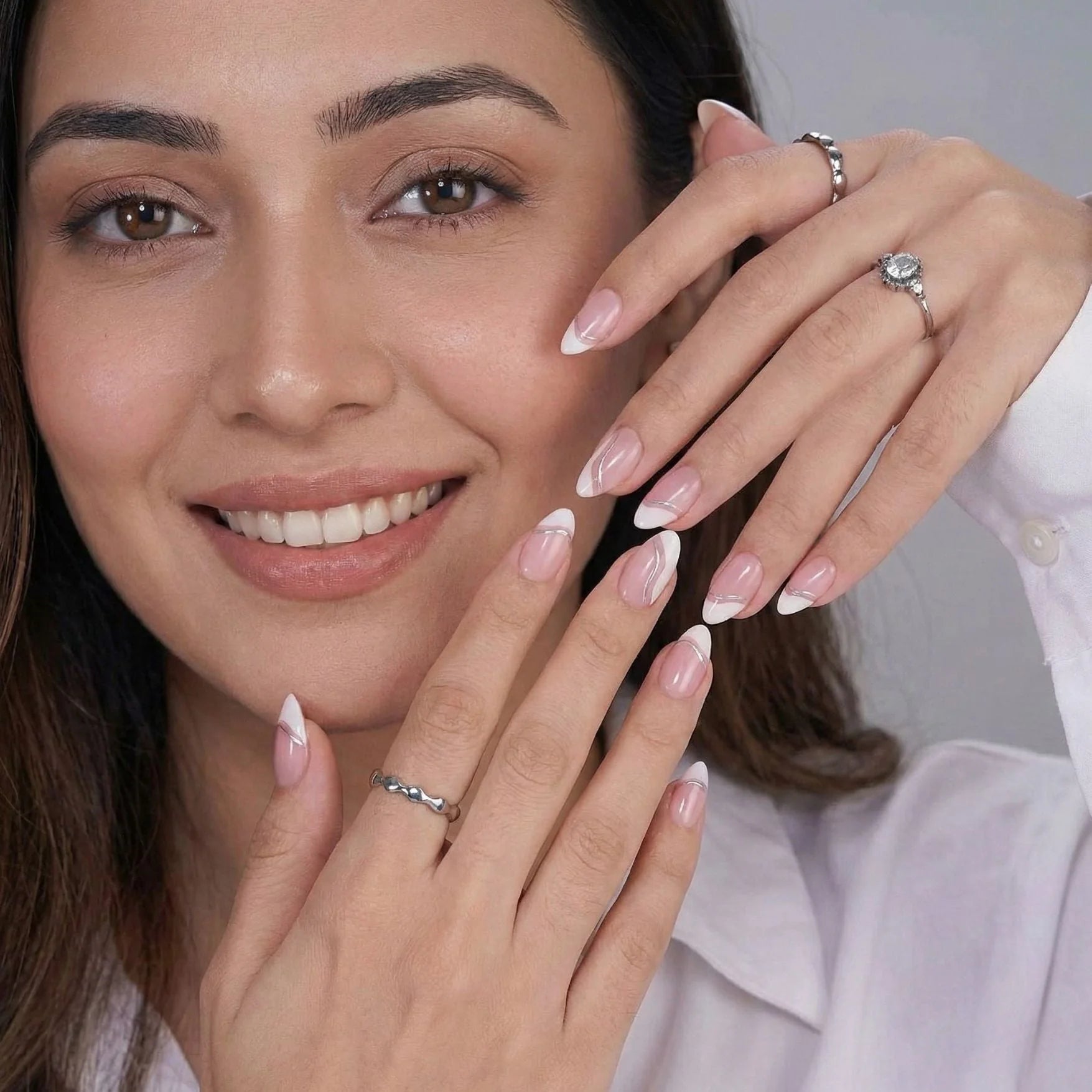 Metallic Merge press-on nails styling – vrouw met Franse amandelvormige kunstnagels en zilveren ringen