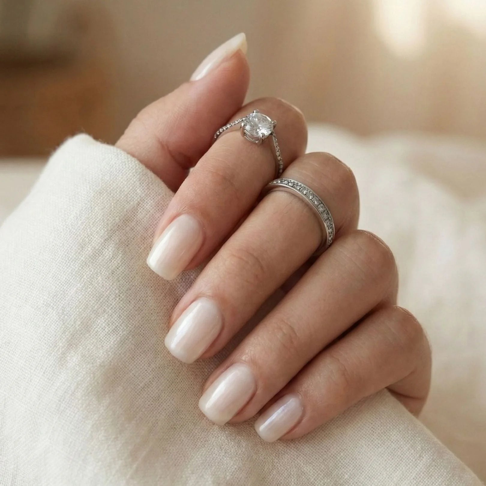 Pure Pearl gelnagels close-up – kort vierkant in pearl nude met witte blouse en zilveren ringen