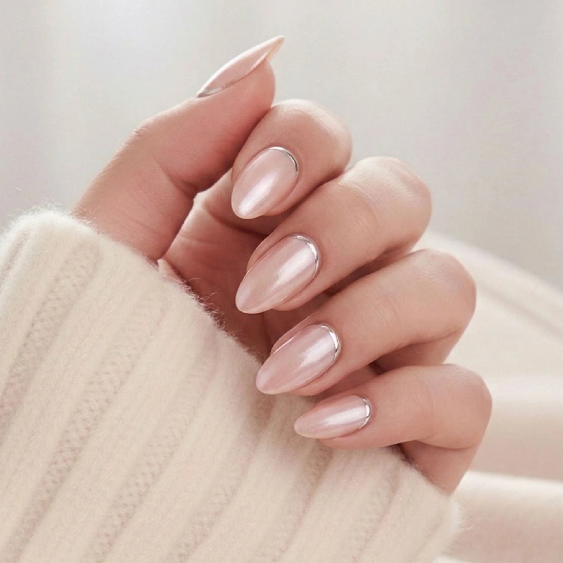 Shimmering Silver press-on nagels – amandelvorm in pearl nude met zilveren rand bij de nagelriem tegen witte gebreide trui