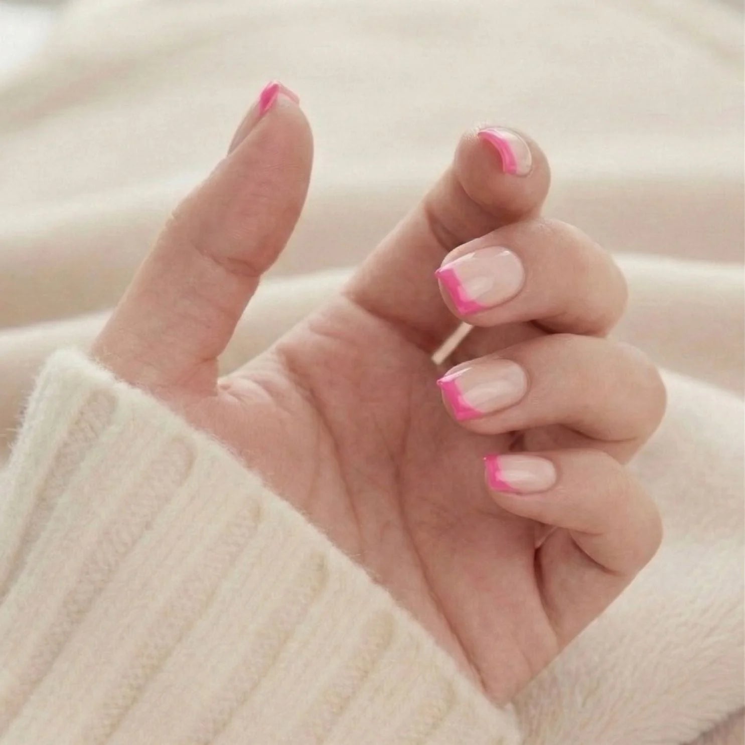 Pixie Pink korte square press-on nagels – roze franse tip van onderaf gezien tegen gebreide trui