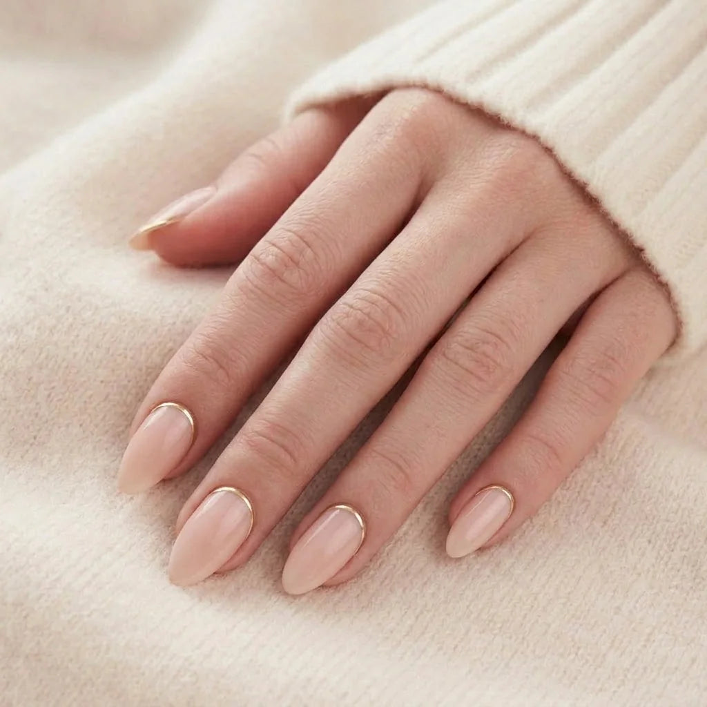 Golden Glimmer nagels op hand – peach nude amandel met gouden detail tegen beige gebreide trui