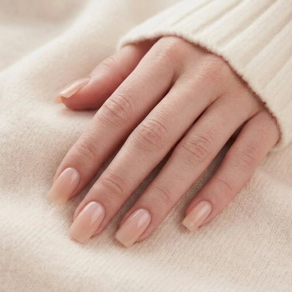 Heavenly Halo kunstnagels close-up – korte vierkante gelnagels in nude met pearl-glans tegen beige gebreide achtergrond