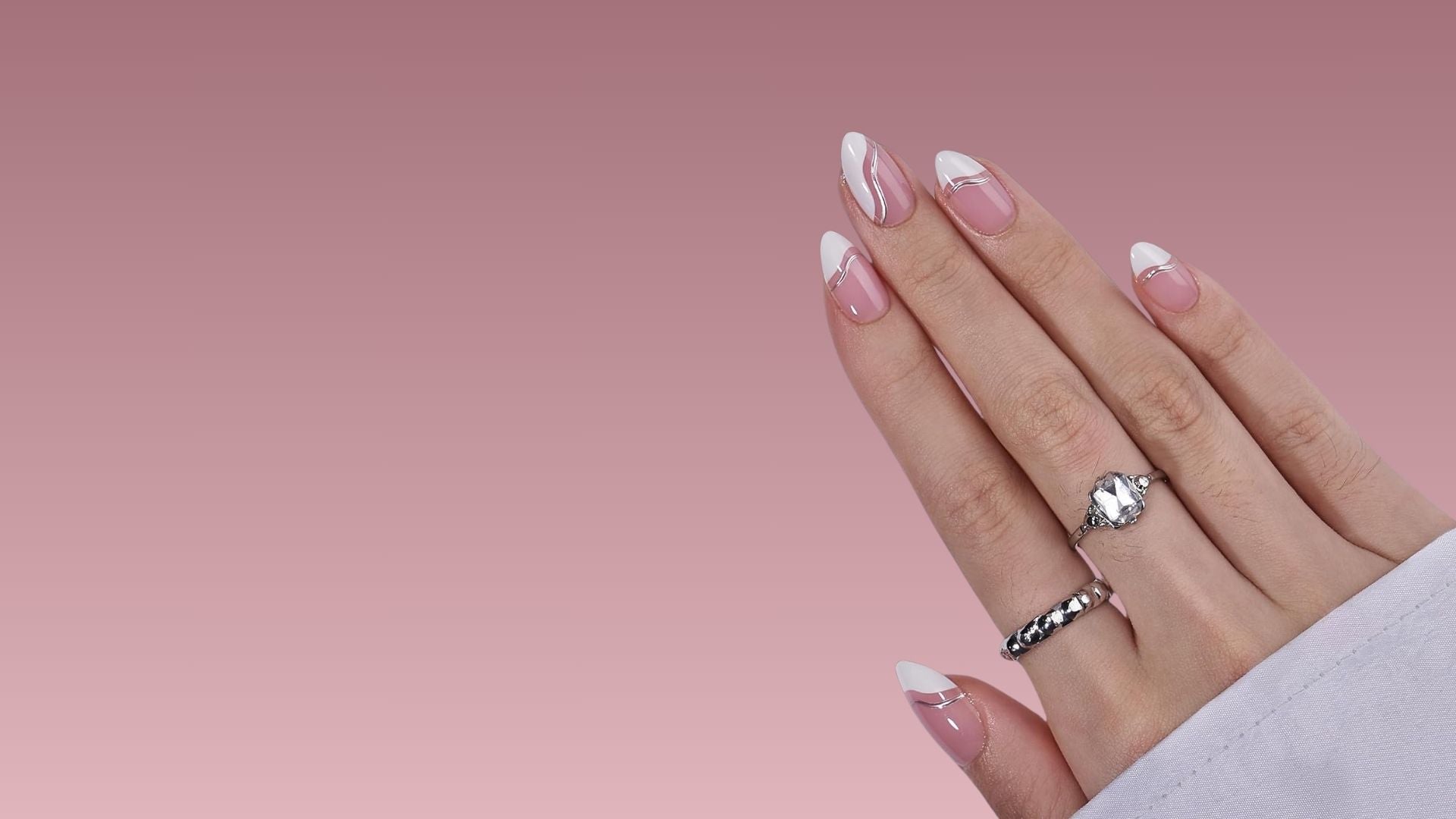 Amandelvormige press-on nagels in roze en wit met modern Frans ontwerp en elegante zilveren details op een hand