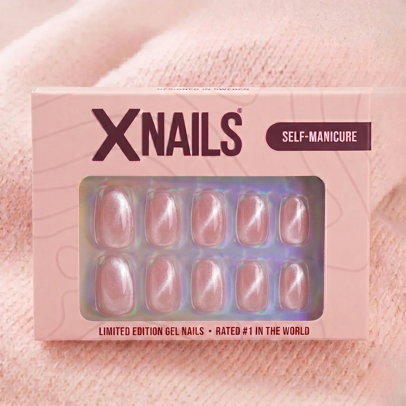 XNails-verpakking met roze chrome almond press-on nagels tegen een roze gebreide achtergrond
