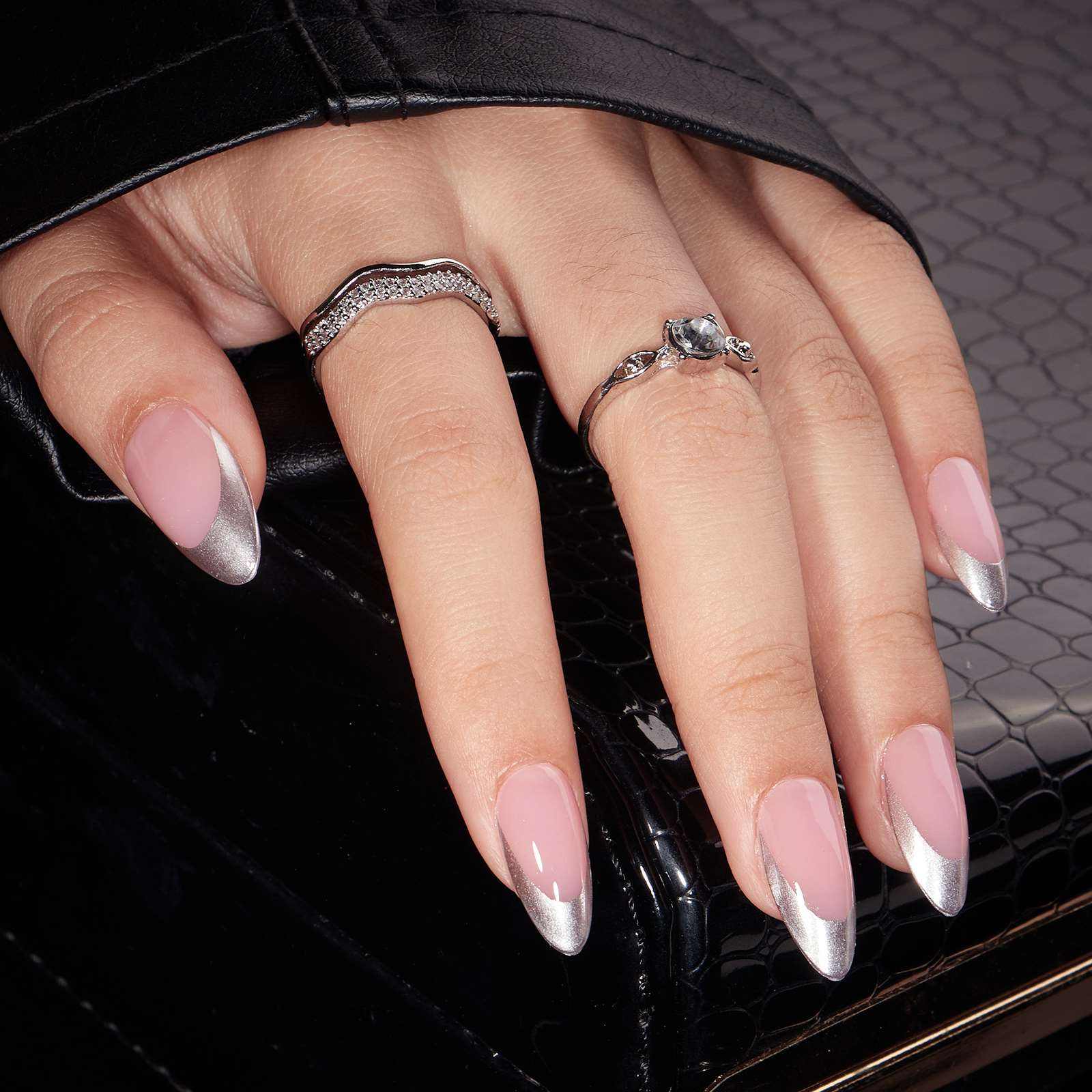 Zilver-chrome franse press-on nagels – amandelvorm op hand met sieradenringen tegen donkere achtergrond