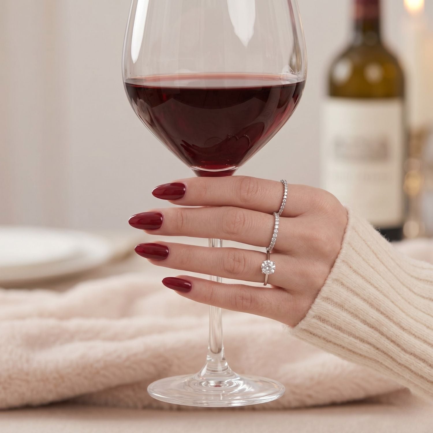 Hand med Ruby Romance press-on naglar i vinröd mandelform håller ett vinglas för en elegant manikyr