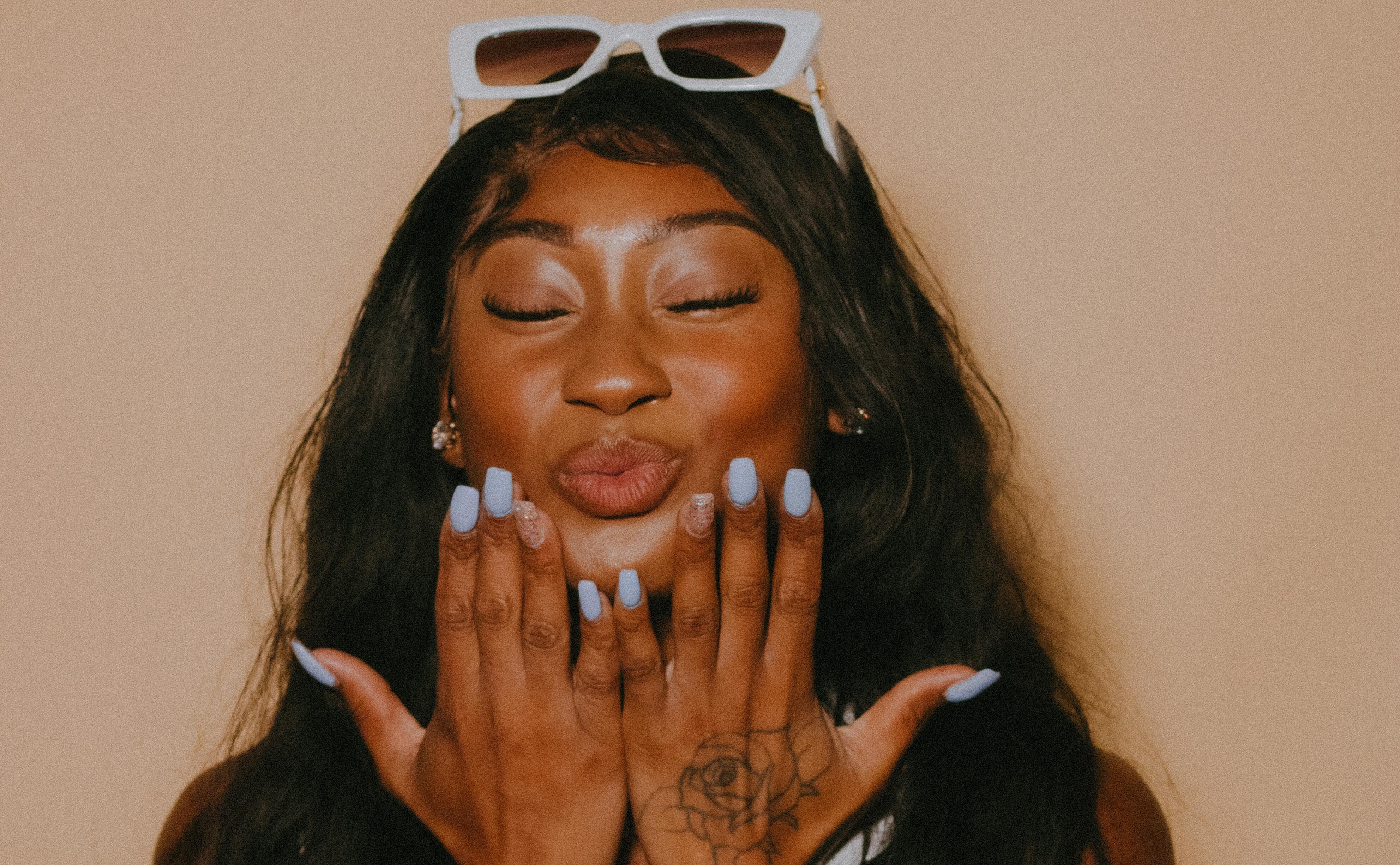 Vrouw met lichtblauwe press-on nagels, sommige met glitter, die een kus blaast met gesloten ogen