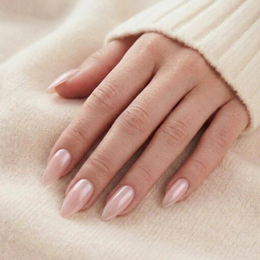 Pinkie Pearl press-on nagels in glanzend melkig roze-nude met parelmoerglans op lange amandelnagels tegen een beige gebreide trui